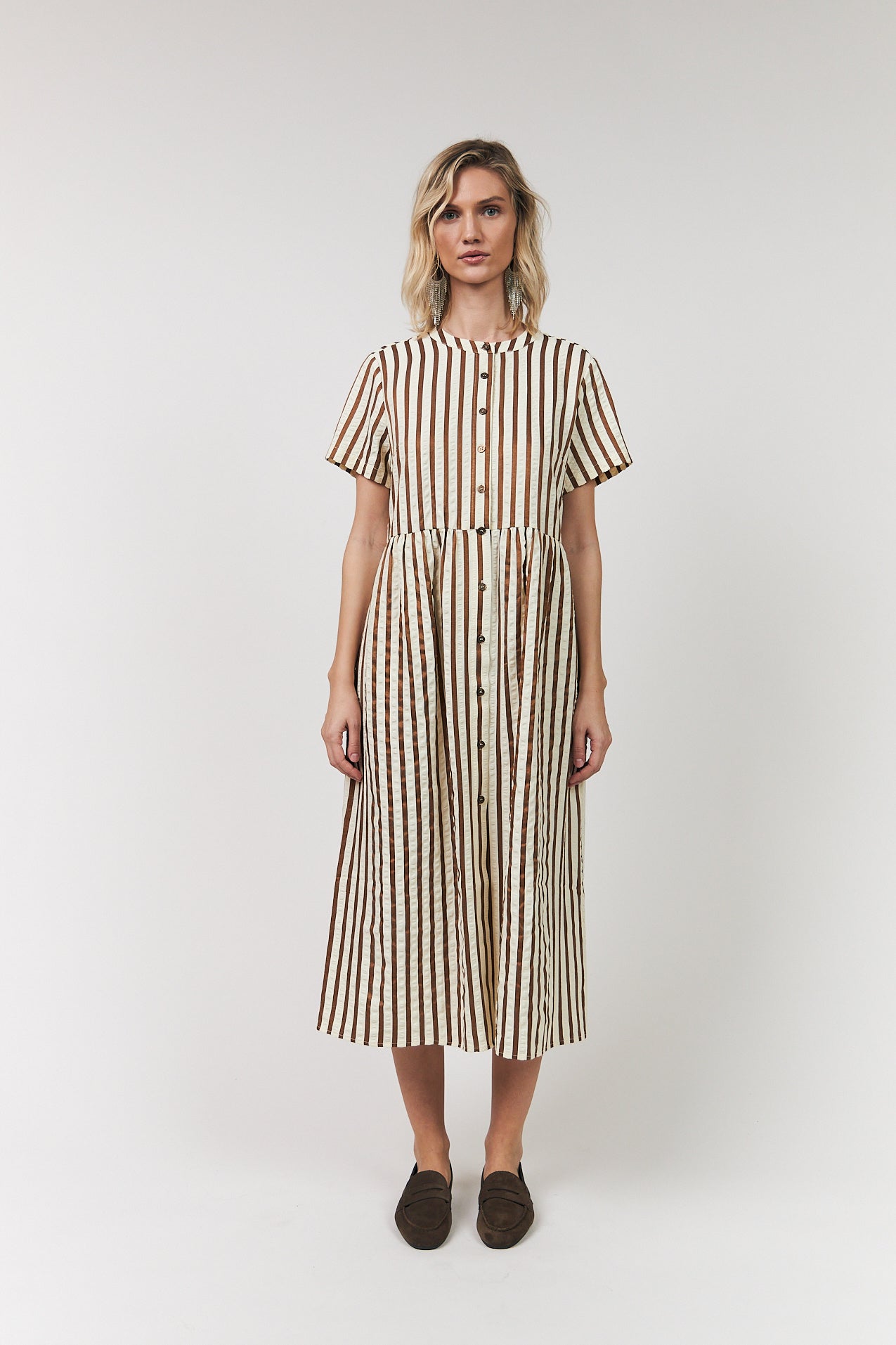 Woman wearing Aliya striped midi dress with button-front closure, round neck, short sleeves and gathered waist, styled with brown loafers.