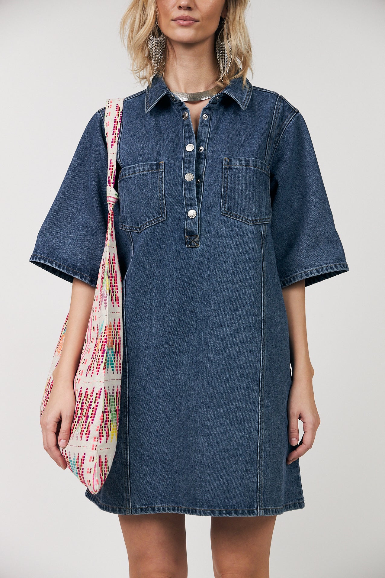Close-up of Mola denim shirt dress showing collar, front button closure with metal buttons and chest pockets, styled with a woven tote bag.