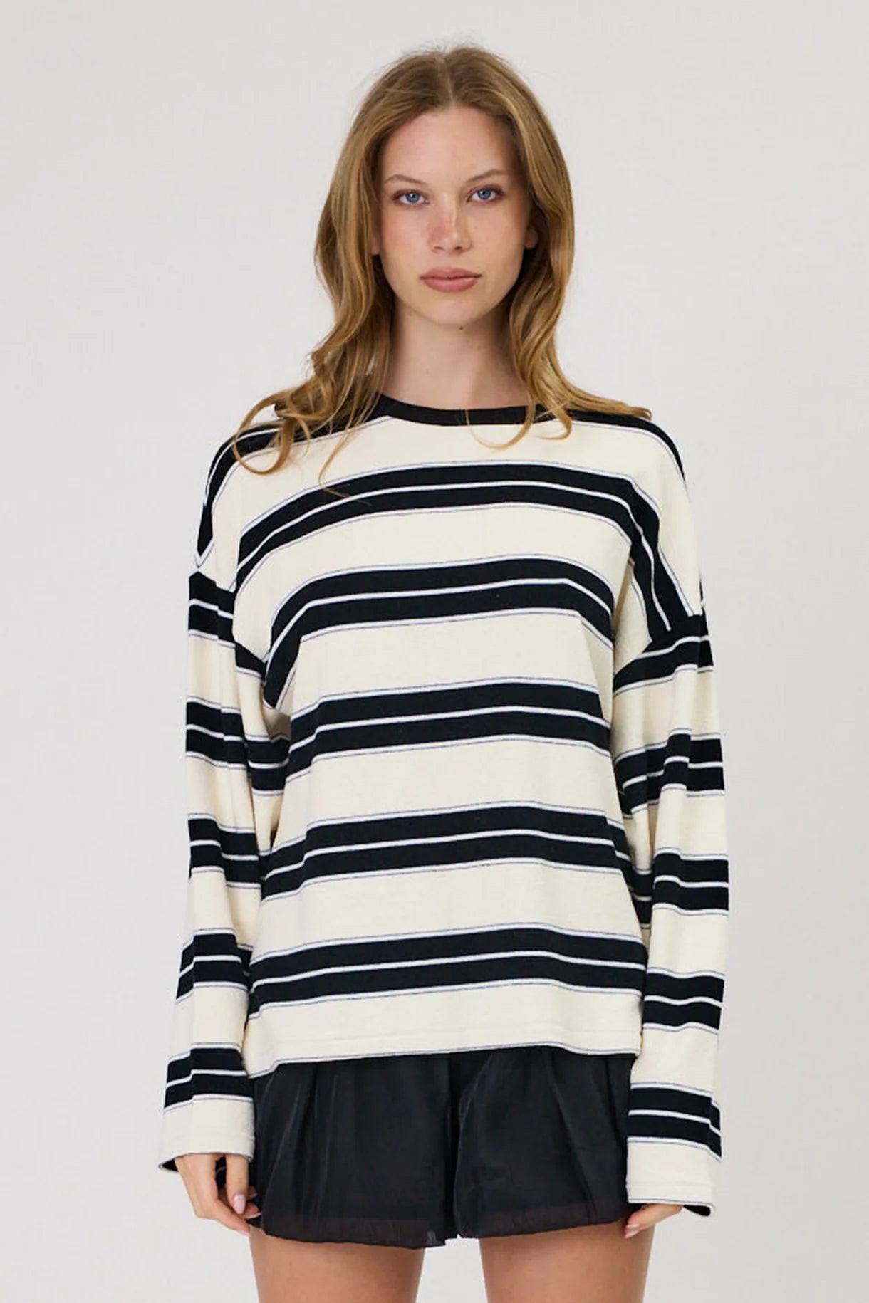 Woman wearing Remain Miller oversized ivory and black striped long sleeve top with black shorts.
