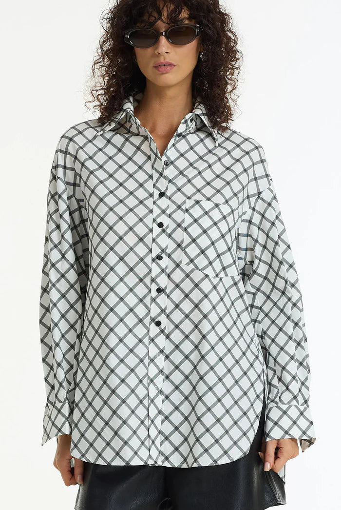Model wearing the Blak Two Makes One Shirt, an oversized white and charcoal check cotton shirt with a classic collar, drop shoulders and curved hem.